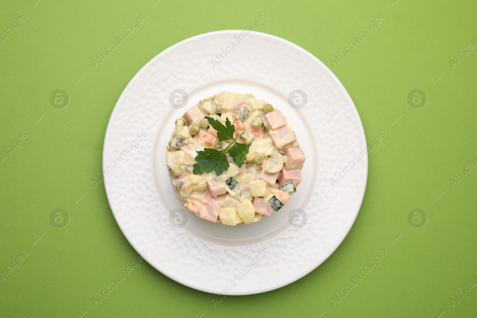 Photo of Tasty Olivier salad with boiled sausage on green table, top view