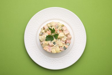 Photo of Tasty Olivier salad with boiled sausage on green table, top view