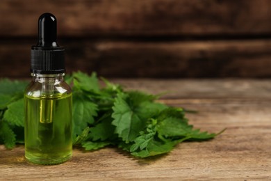 Photo of Glass bottle of nettle oil with dropper and leaves on wooden table, closeup. Space for text]