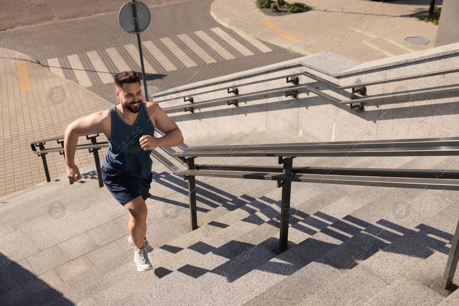 Photo of Smiling man running up stairs outdoors on sunny day, above view. Space for text