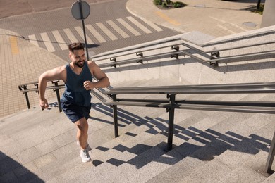 Smiling man running up stairs outdoors on sunny day, above view. Space for text