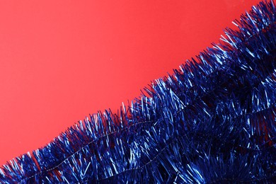 Photo of Bright blue tinsel on red background, top view. Space for text