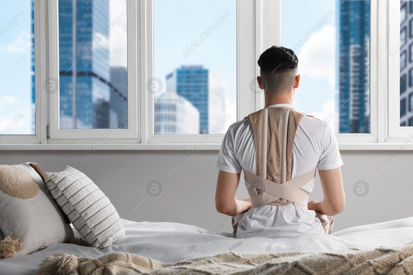 Photo of Man with orthopedic corset sitting in room, back view