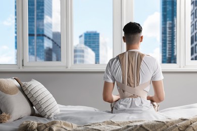 Man with orthopedic corset sitting in room, back view