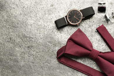 Photo of Stylish burgundy bow tie, cufflinks and wristwatch on grey background, flat lay. Space for text