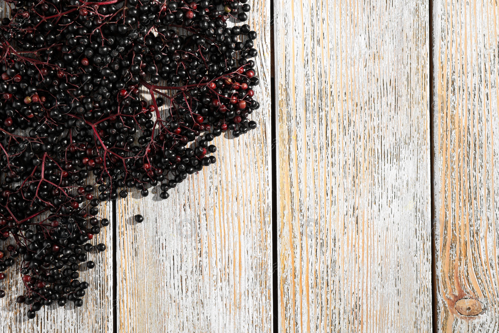 Photo of Black elderberries (Sambucus) on old wooden table, flat lay. Space for text