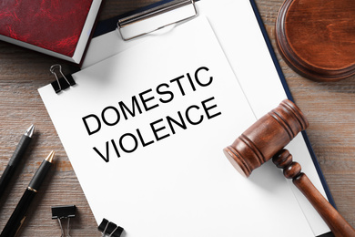 Photo of Clipboard with words DOMESTIC VIOLENCE and gavel on wooden table, flat lay