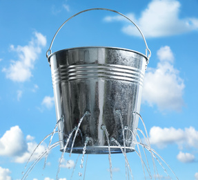 Image of Leaky bucket with water against blue sky