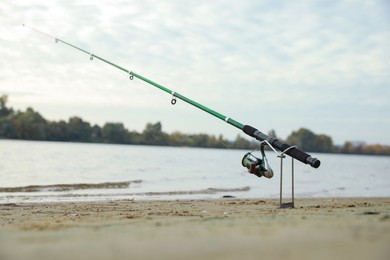 Photo of Fishing rod with reel on sand near river, space for text