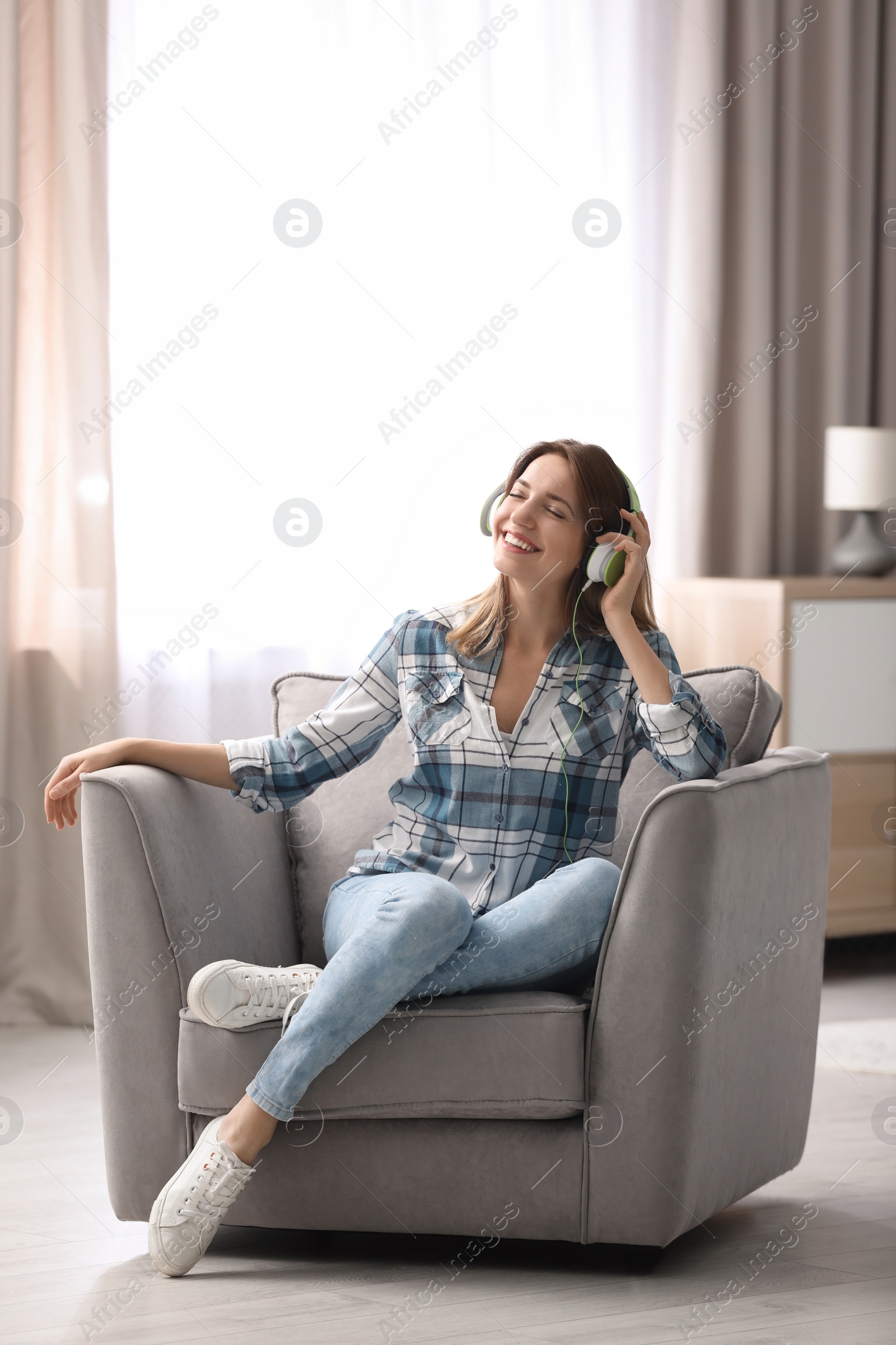 Photo of Young woman with headphones resting in armchair at home