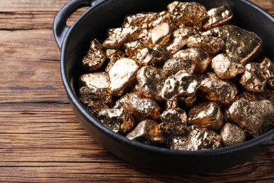 Photo of Pan of gold nuggets on wooden table, closeup