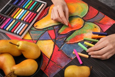 Photo of Woman drawing pears on paper with soft pastels at wooden table, closeup