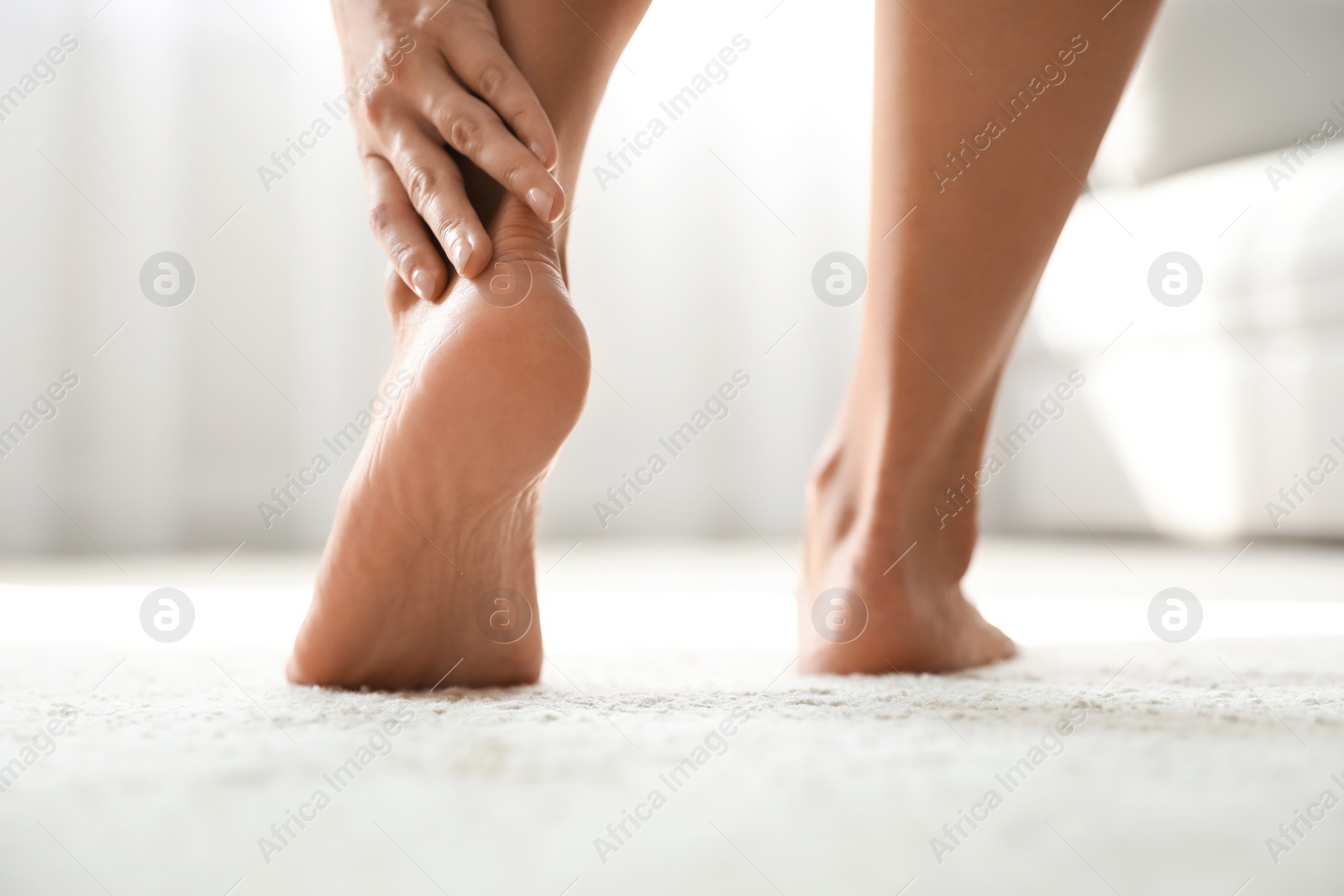 Photo of Young woman suffering from pain in foot indoors, closeup