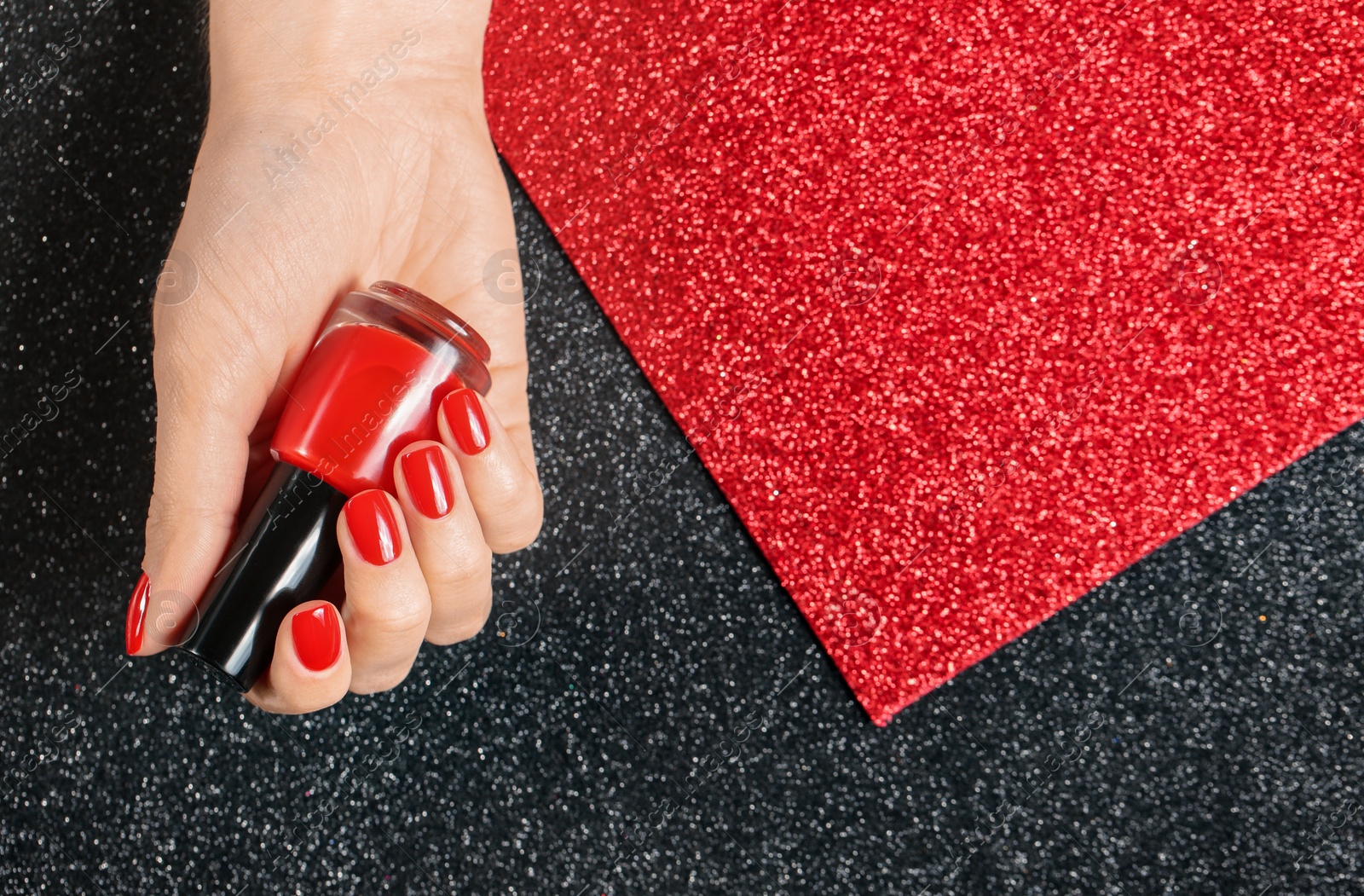 Photo of Woman holding bottle of red nail polish in manicured hand on color background, top view. Space for text