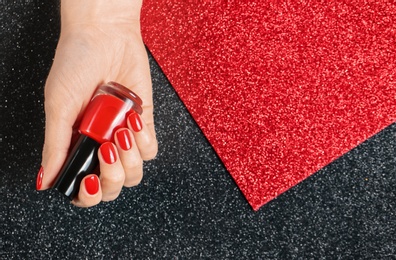 Woman holding bottle of red nail polish in manicured hand on color background, top view. Space for text