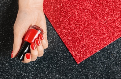 Photo of Woman holding bottle of red nail polish in manicured hand on color background, top view. Space for text