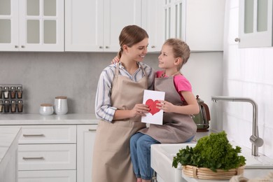 Little daughter congratulating mom with greeting card in kitchen. Happy Mother's Day