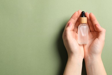 Woman holding bottle with serum on olive background, top view. Space for text