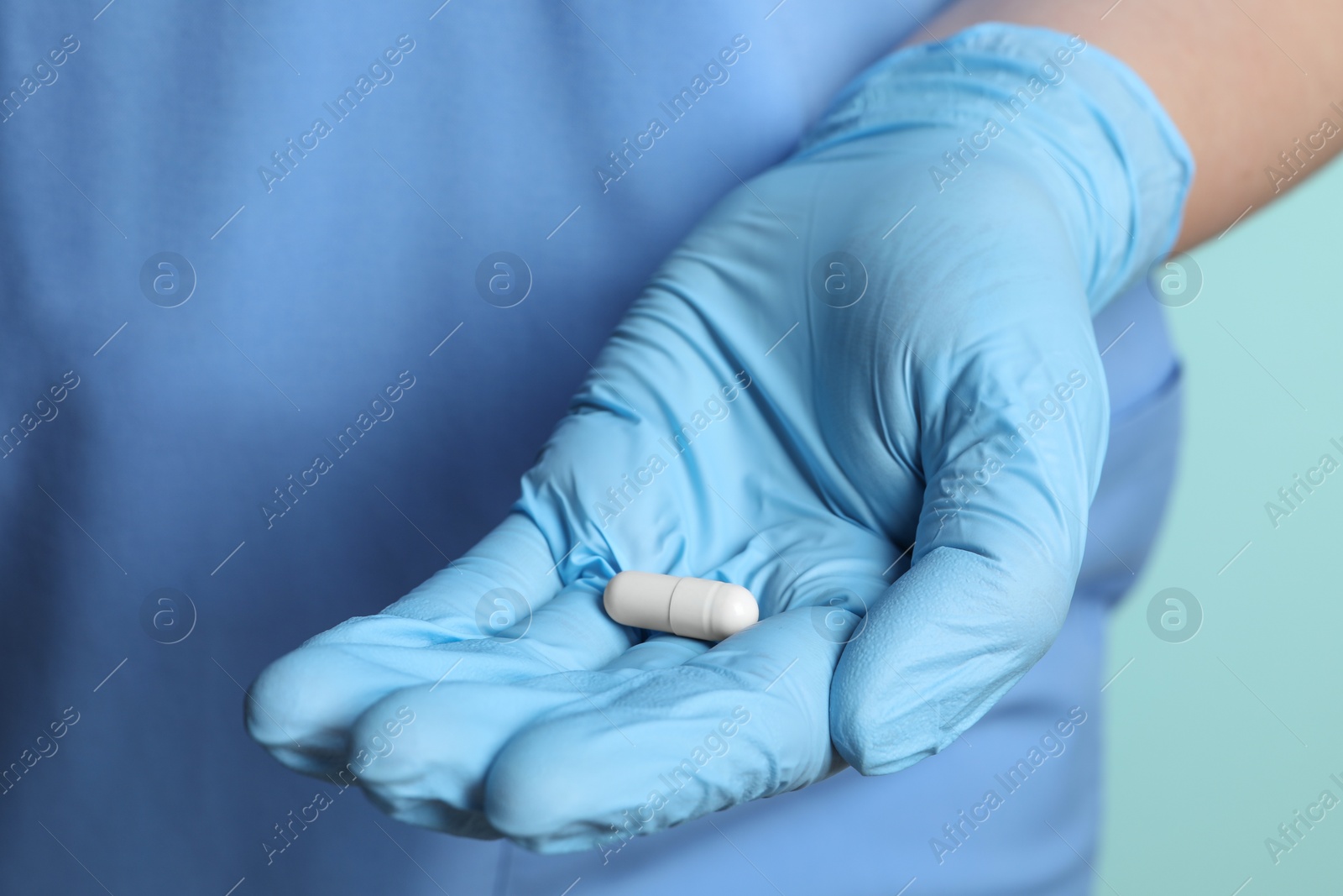 Photo of Doctor in medical glove holding pill on turquoise background, closeup