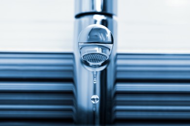 Water drops falling down from tap on blurred background, closeup