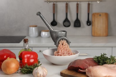 Metal meat grinder with chicken mince and products on white table in kitchen