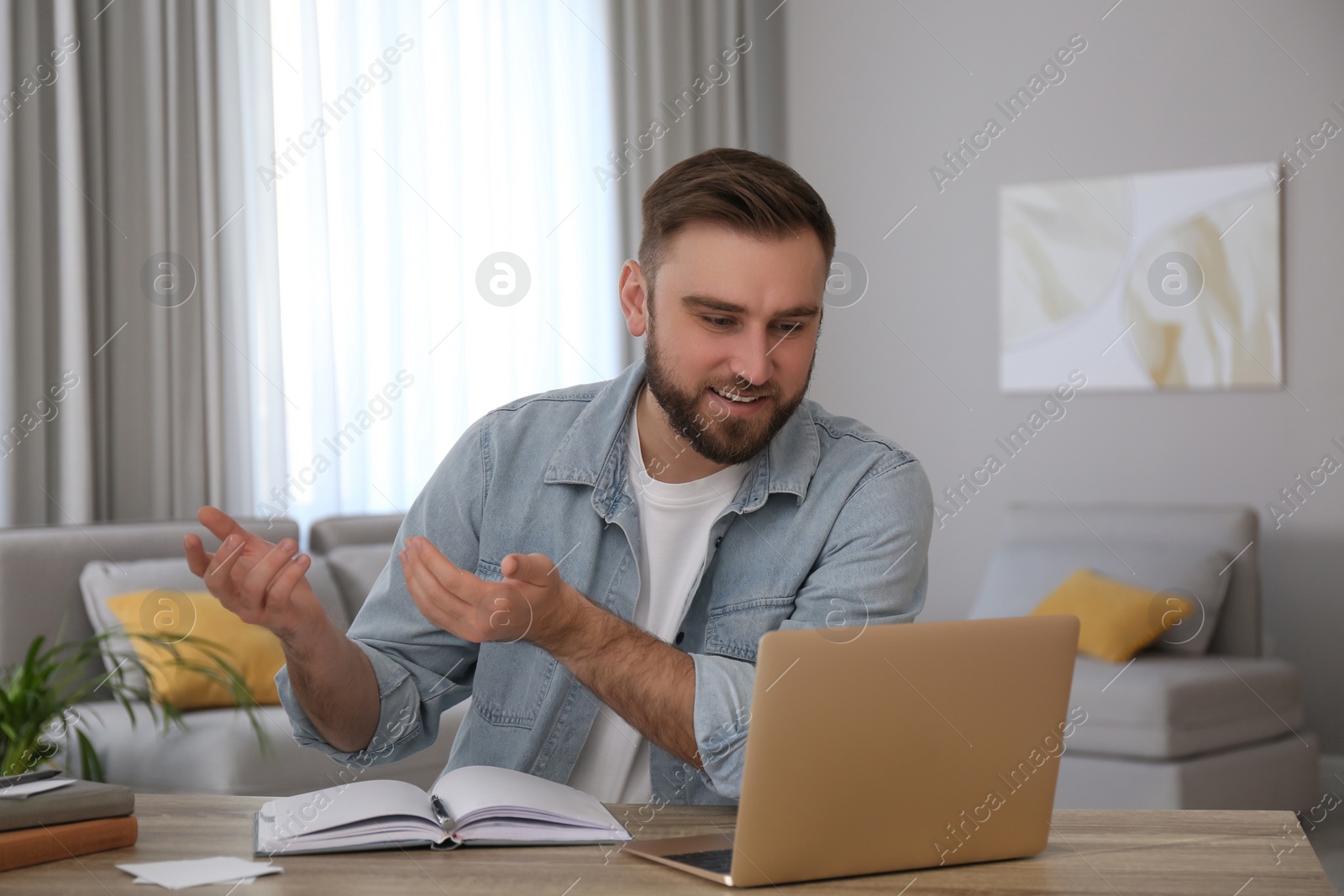 Photo of Young man watching online webinar at table indoors