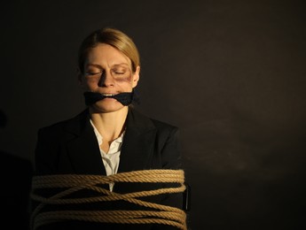 Photo of Woman with bruises tied up and taken hostage on dark background. Space for text
