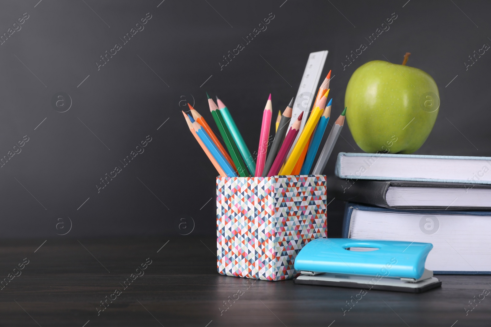 Photo of Apple and school stationery on black wooden table, space for text. Doing homework