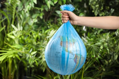 Photo of Woman holding globe in plastic bag against green leaves, closeup. Environmental conservation
