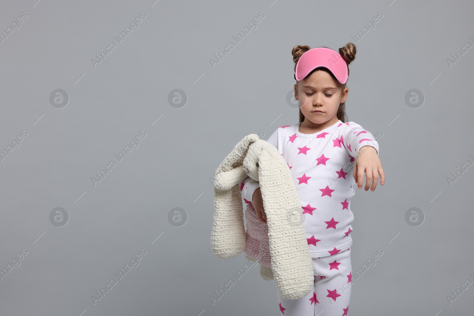 Photo of Girl in pajamas and sleep mask with toy bunny sleepwalking on gray background, space for text