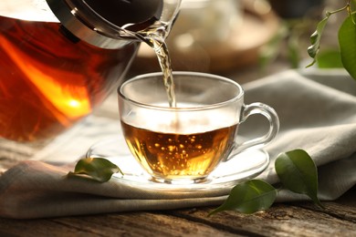 Photo of Pouring tea into cup on wooden table, closeup