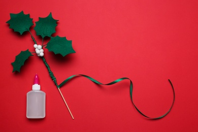 Photo of Handmade mistletoe branch and glue on red background, flat lay