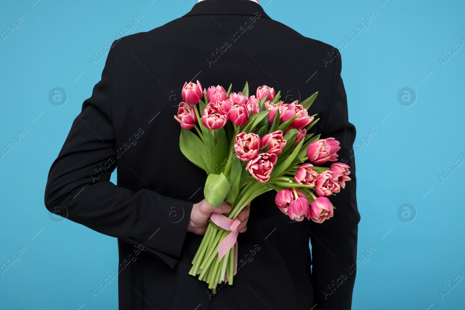 Photo of Man hiding beautiful bouquet on light blue background, back view