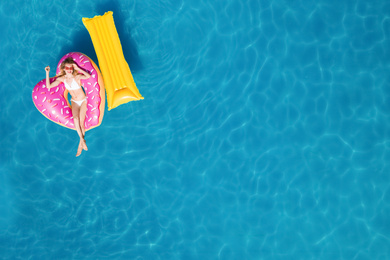 Image of Happy woman with inflatable mattress and ring in swimming pool, top view. Summer vacation