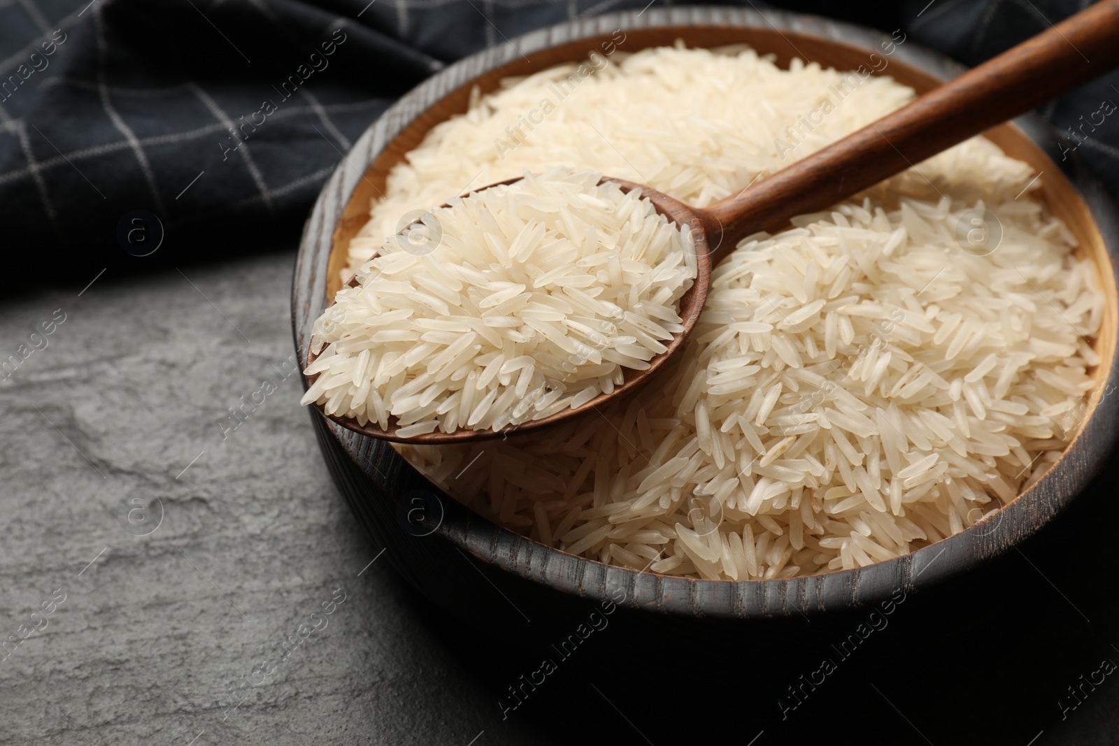 Photo of Raw basmati rice in bowl and spoon on black table, closeup