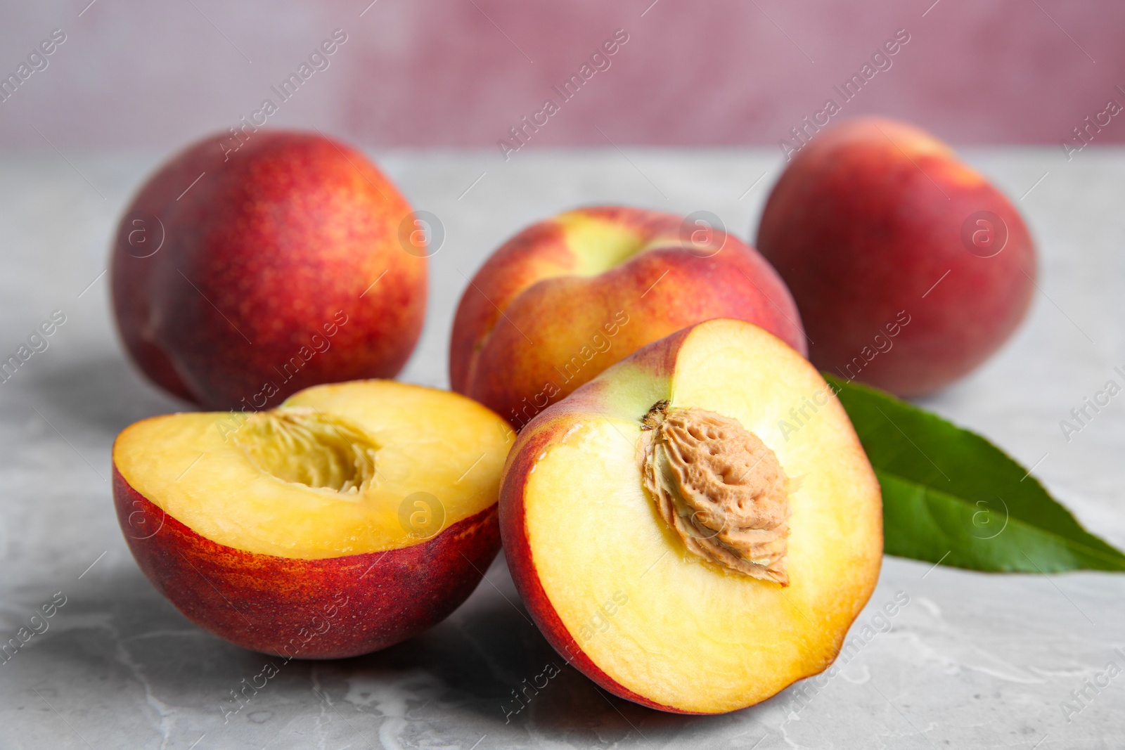 Photo of Cut and whole juicy peaches and leaves on grey table