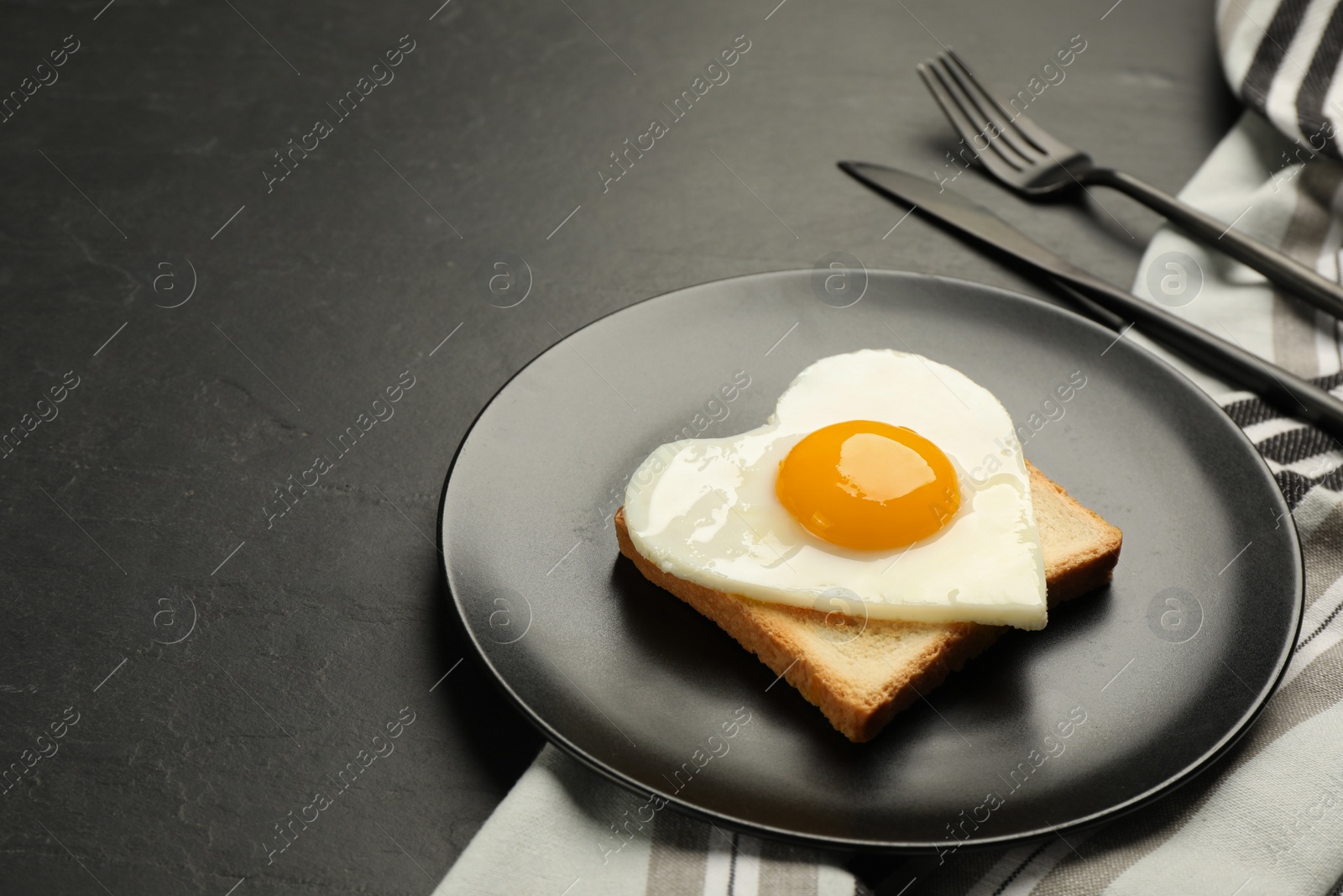 Photo of Tasty fried egg in shape of heart with toast served on dark grey table. Space for text