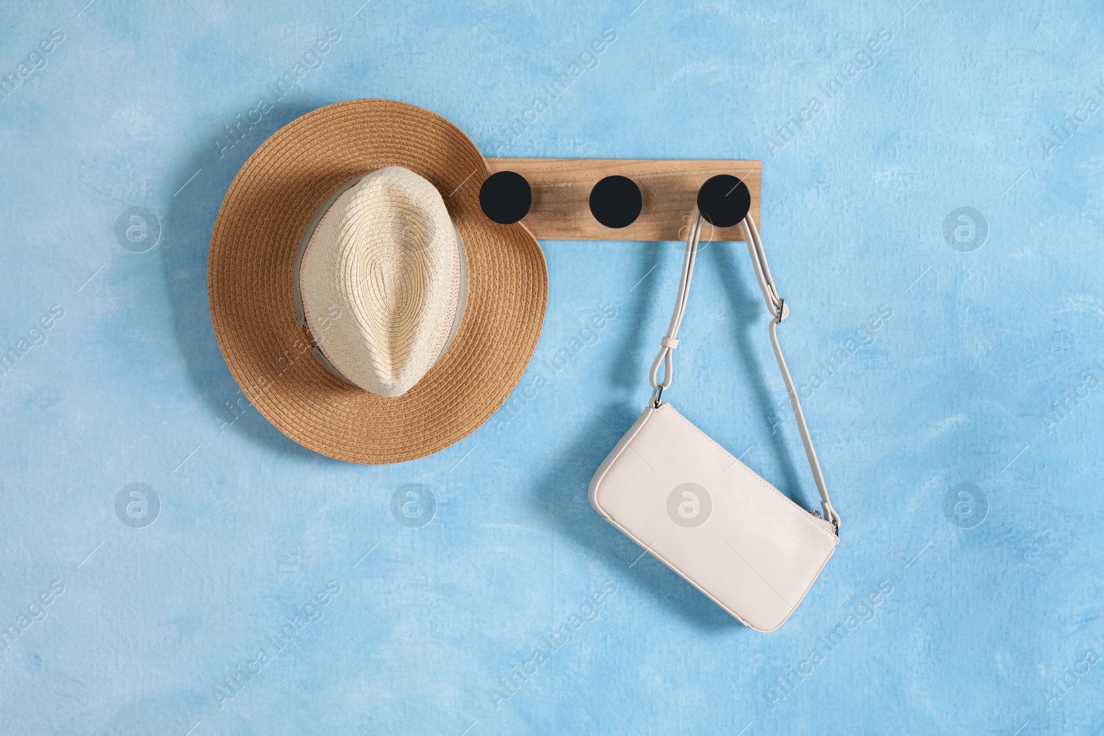 Photo of Wooden rack with hat and bag on light blue wall
