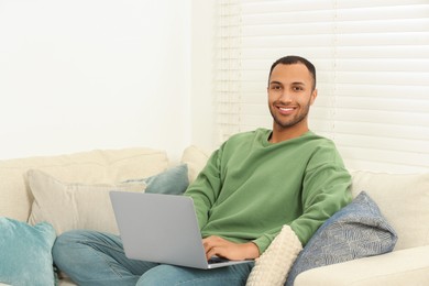 Photo of Smiling African American man with laptop on sofa in room