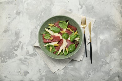 Delicious bresaola salad in bowl served on light grey textured table, flat lay