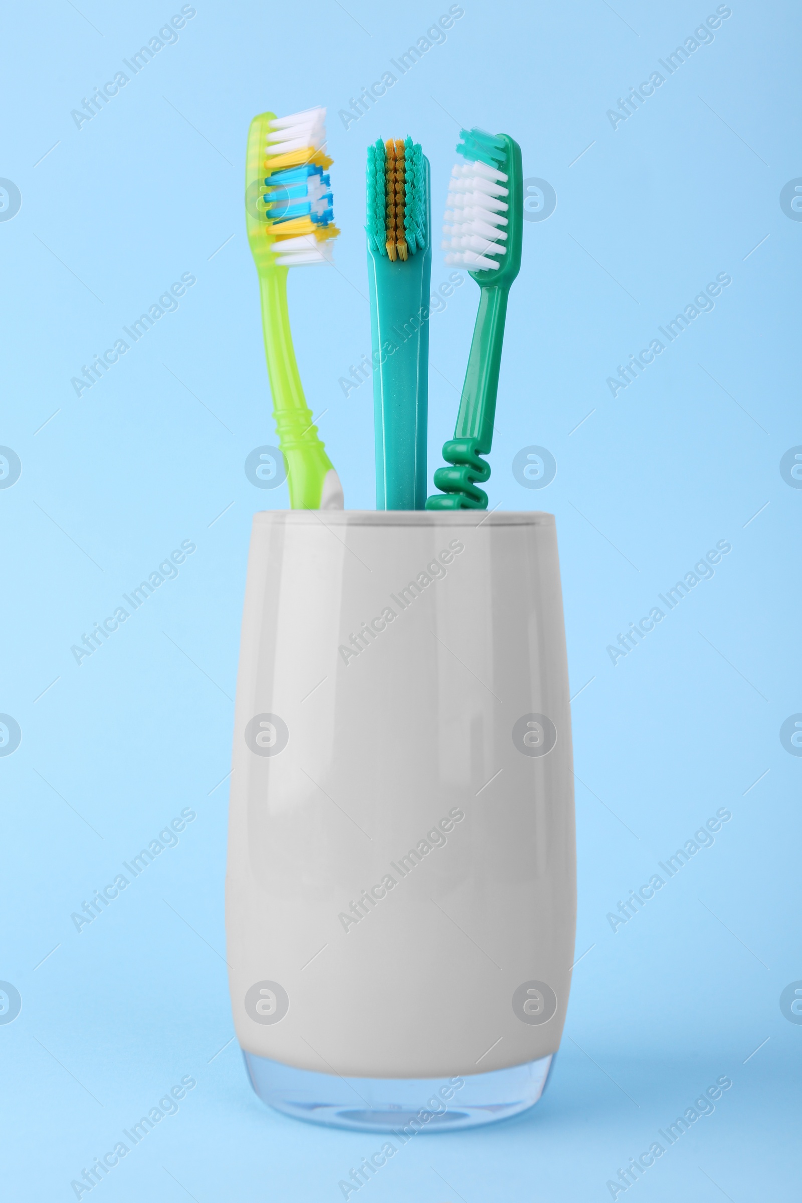 Photo of Different toothbrushes in holder on light blue background