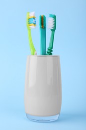 Photo of Different toothbrushes in holder on light blue background