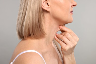 Woman touching her neck on grey background, closeup