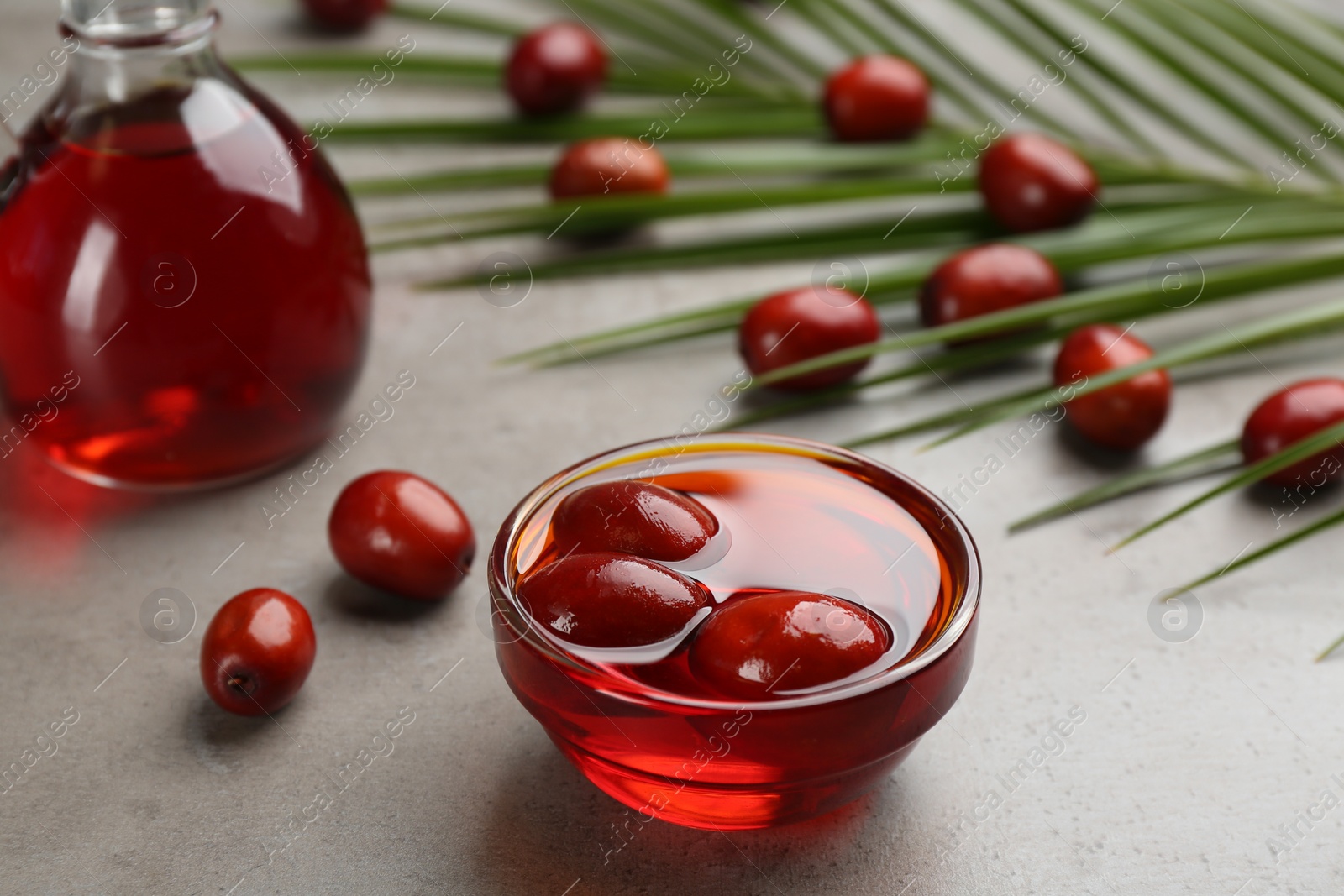 Photo of Palm oil in glass bowl with fruits and tropical leaf on grey table