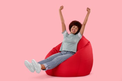 Beautiful young woman sitting on beanbag chair against pink background