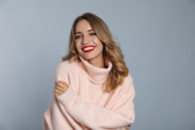 Photo of Happy young woman wearing warm sweater on grey background. Christmas celebration