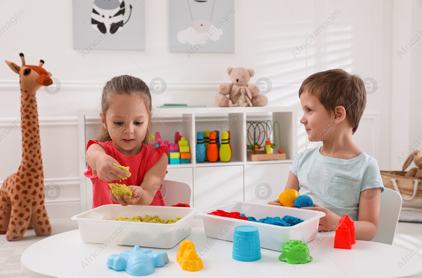 Photo of Cute little children playing with bright kinetic sand at table in room