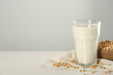 Photo of Glass with fresh soy milk and grains on white wooden table. Space for text