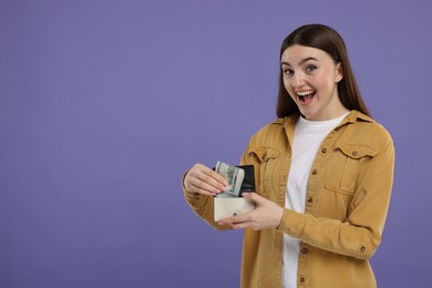 Photo of Excited woman putting dollar banknotes into wallet on purple background, space for text