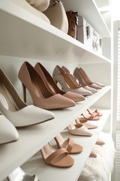 Photo of Different stylish women's shoes on shelving unit in dressing room